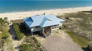 Et strandhus med skråt tag, en overdækket veranda og en grusvej.
