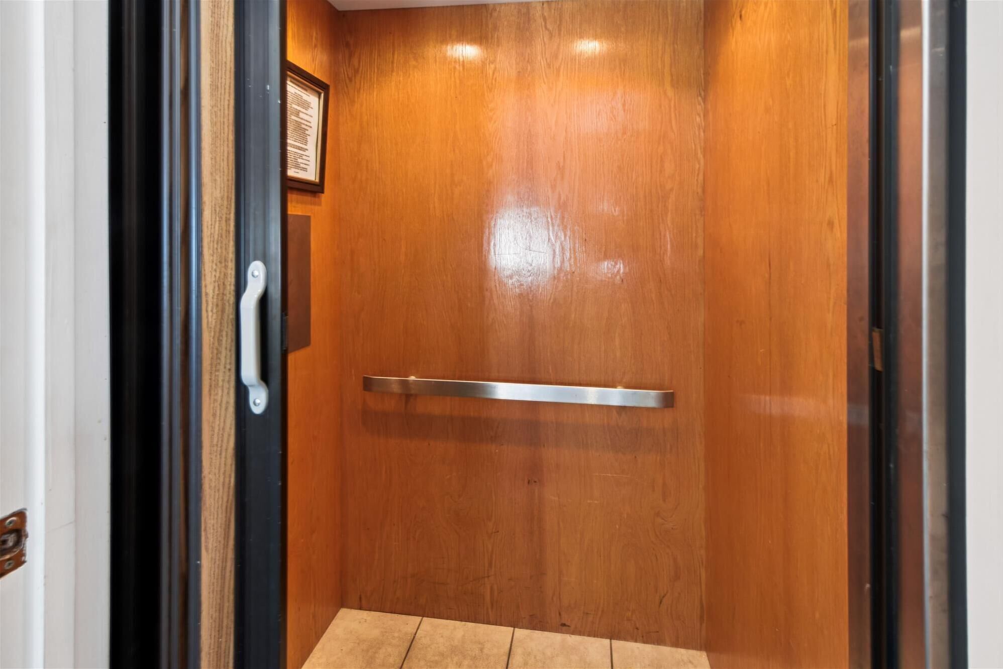 A wooden elevator door with a metallic handle and a small plaque on the wall.