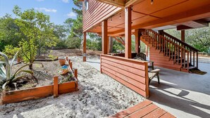 Une terrasse en bois couverte, dotée d’un escalier, d’un espace salon extérieur et d’un jardin agrémenté de plantes et d’un vase décoratif.