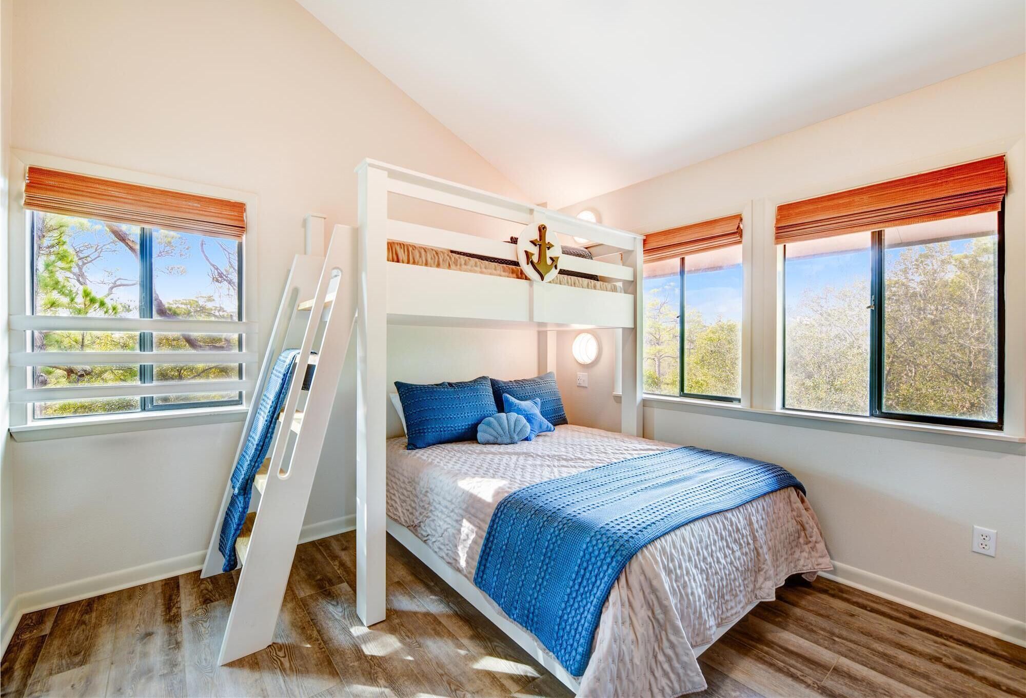 Habitación con literas, una escalera, dos ventanas con persianas y vista a árboles.