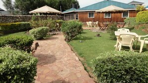Un sendero de piedra conduce a una casa de madera con techo azul, rodeada de setos cuidados y un césped.
