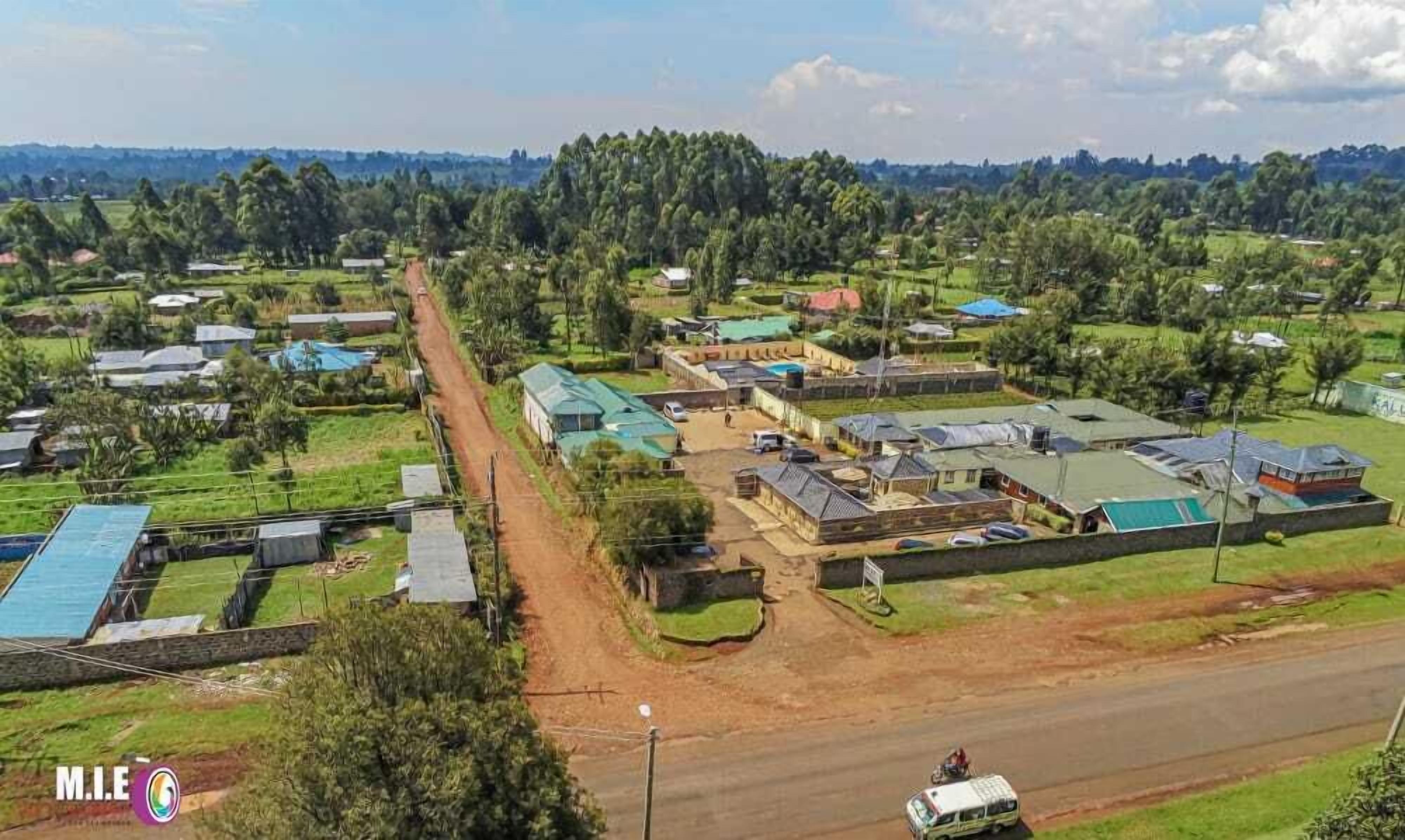 Vista aérea de una zona rural con casas dispersas, un camino de tierra y un gran campo verde.