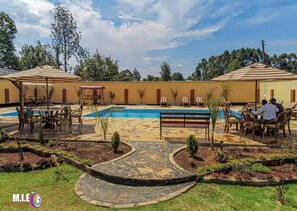 A pool area with lounge chairs and umbrellas, surrounded by a landscaped garden and a stone pathway. - Hills Country Lodge Kericho (Kericho)