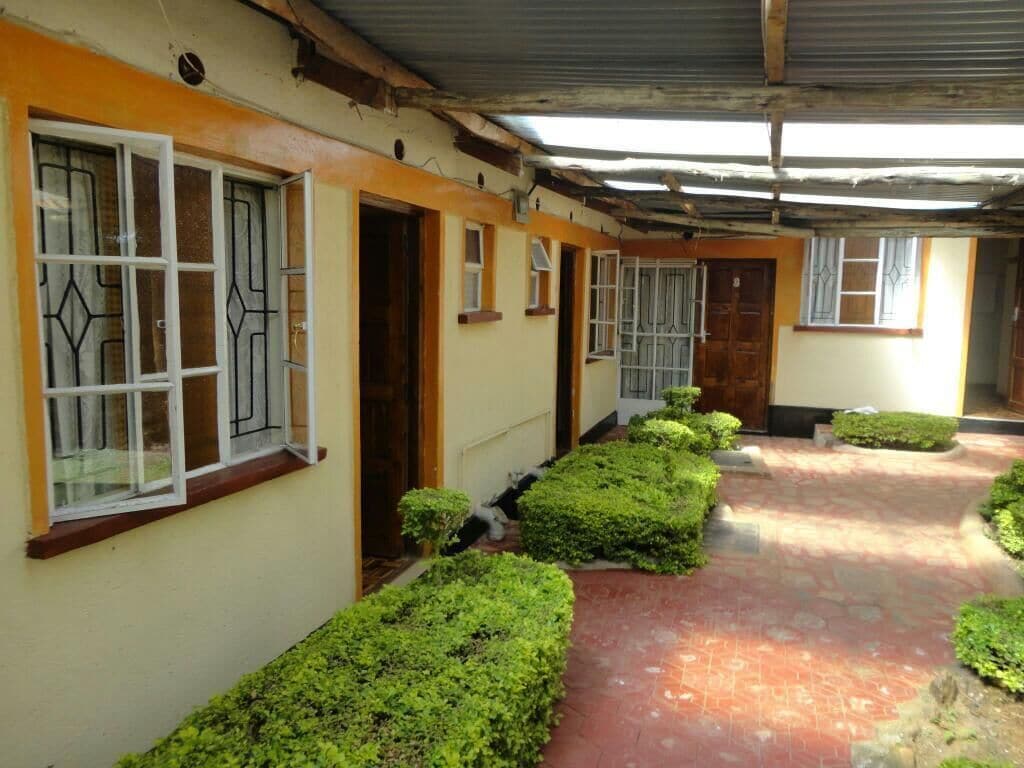 A corridor with a tiled floor, a covered roof, and neatly trimmed hedges along the path.