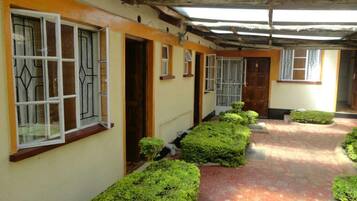 A corridor with a tiled floor, a covered roof, and neatly trimmed hedges along the path.