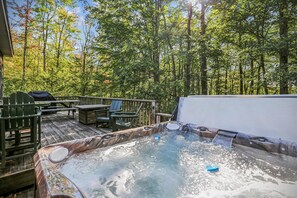 A hot tub surrounded by a wooden deck, with a table and chairs nearby.