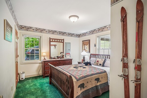 A bedroom with a wooden bed, a dresser, a mirror, and a quilt with animal prints.