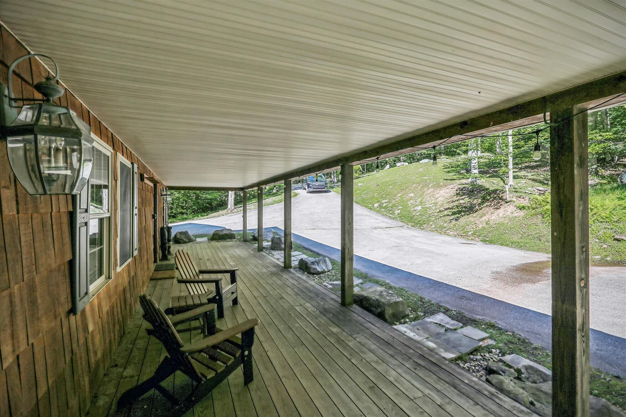 A covered porch with wooden benches and a view of a road and greenery.