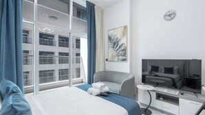 A hotel room with a bed, a chair, a TV, and a window with curtains.
