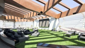 A modern outdoor lounge area with a curved seating arrangement, artificial grass, and a high ceiling with geometric beams.