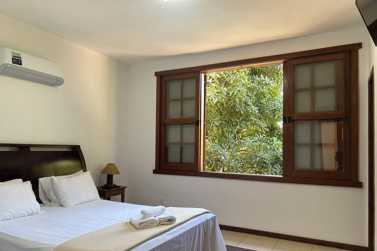 Une chambre à coucher avec un lit, une table de chevet, une lampe et une fenêtre donnant sur un paysage verdoyant.