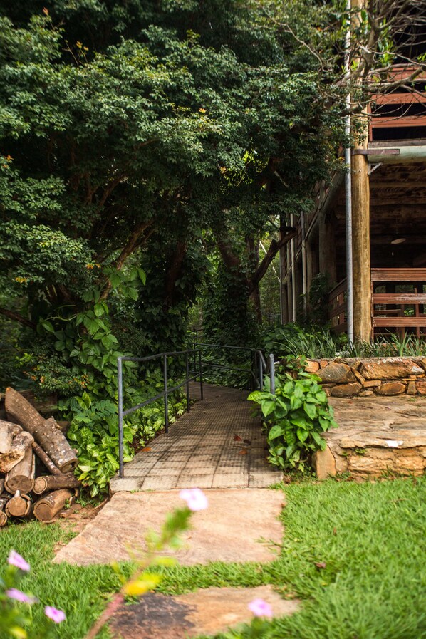 A pathway leading to a building surrounded by dense greenery and a stone wall. - Pousada Fazenda Monjolos (Santana do Riacho)