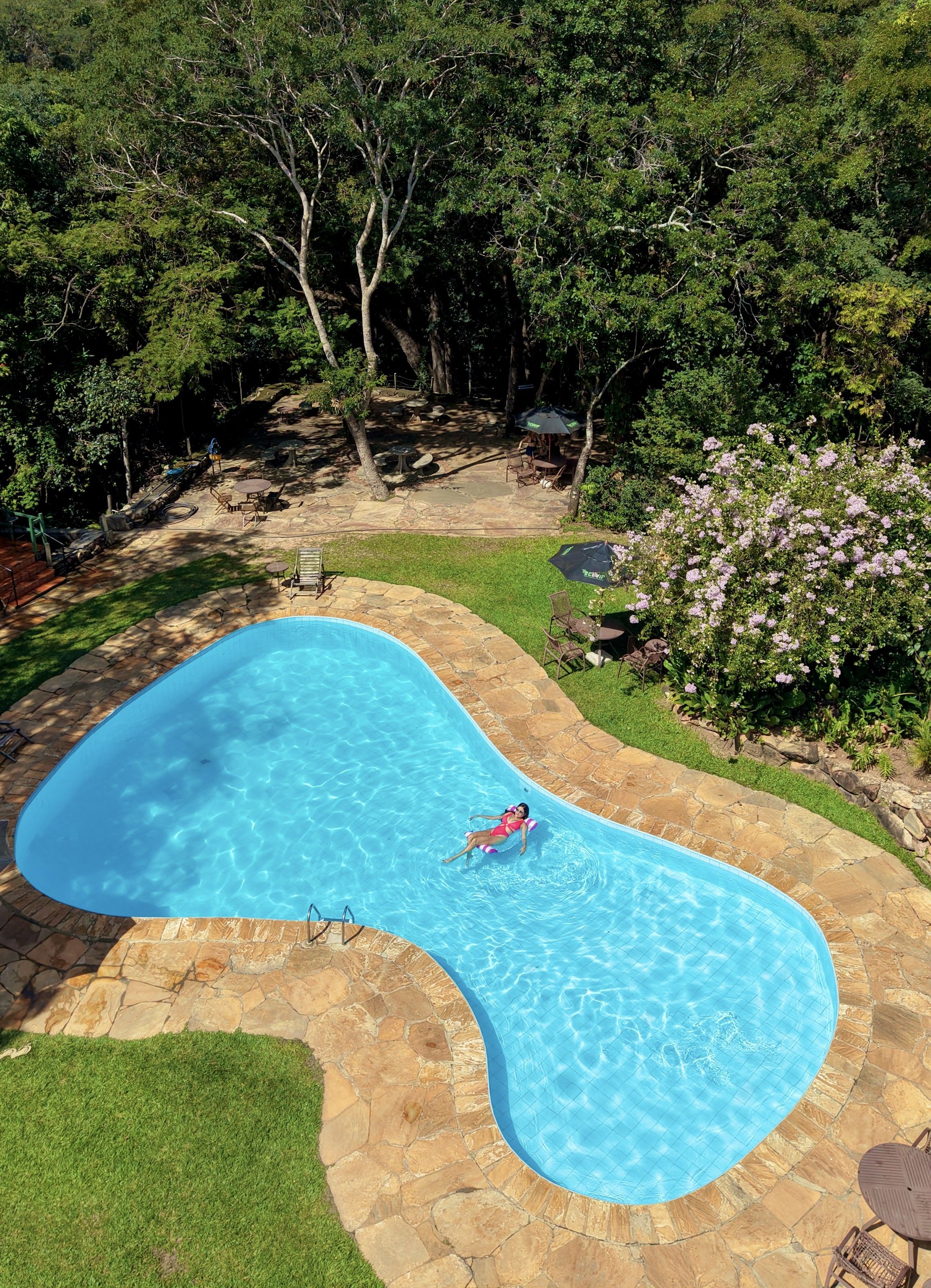 A swimming pool with a stone deck, surrounded by a grassy area and trees.