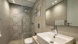 Un baño moderno con ducha envuelta en vidrio, lavamanos blanco y un inodoro.
