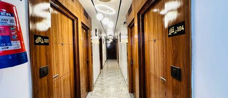 A hotel corridor with wooden doors, numbered room signs, a marble floor, and a fire extinguisher on the wall.