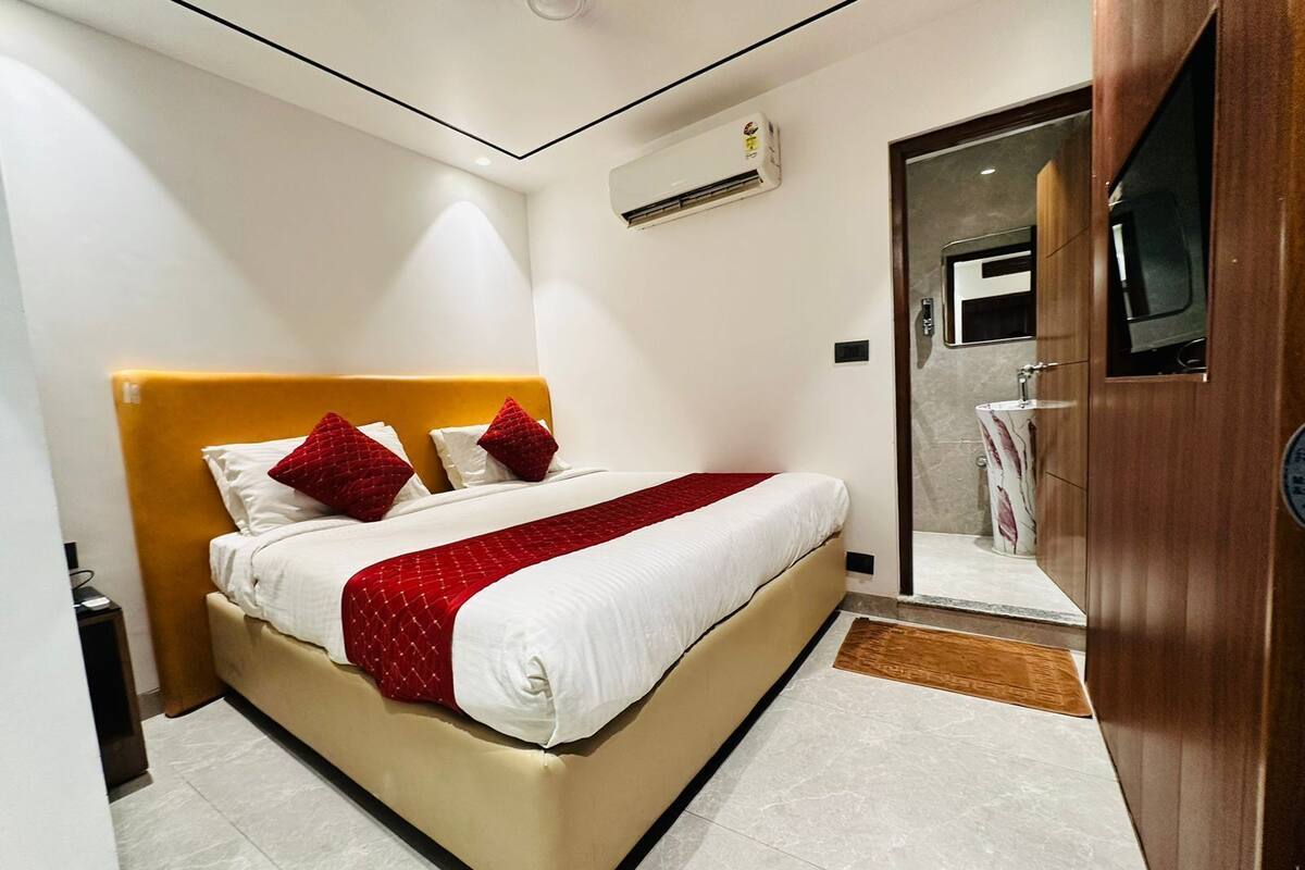 A hotel room with a bed, a wooden headboard, a red and white bedspread, and a bathroom with a mirror and sink.