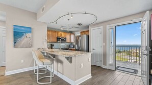 A modern kitchen with a large island, wooden cabinets, and a view of the ocean through the sliding glass door.