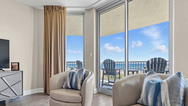 A modern hotel room with a balcony, leather armchairs, a flat-screen TV, and a view of the beach.