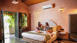 Un dormitorio con una cama grande, un escritorio y una silla. Hay una ventana con cortinas, un equipo de aire acondicionado y un aplique en la pared.