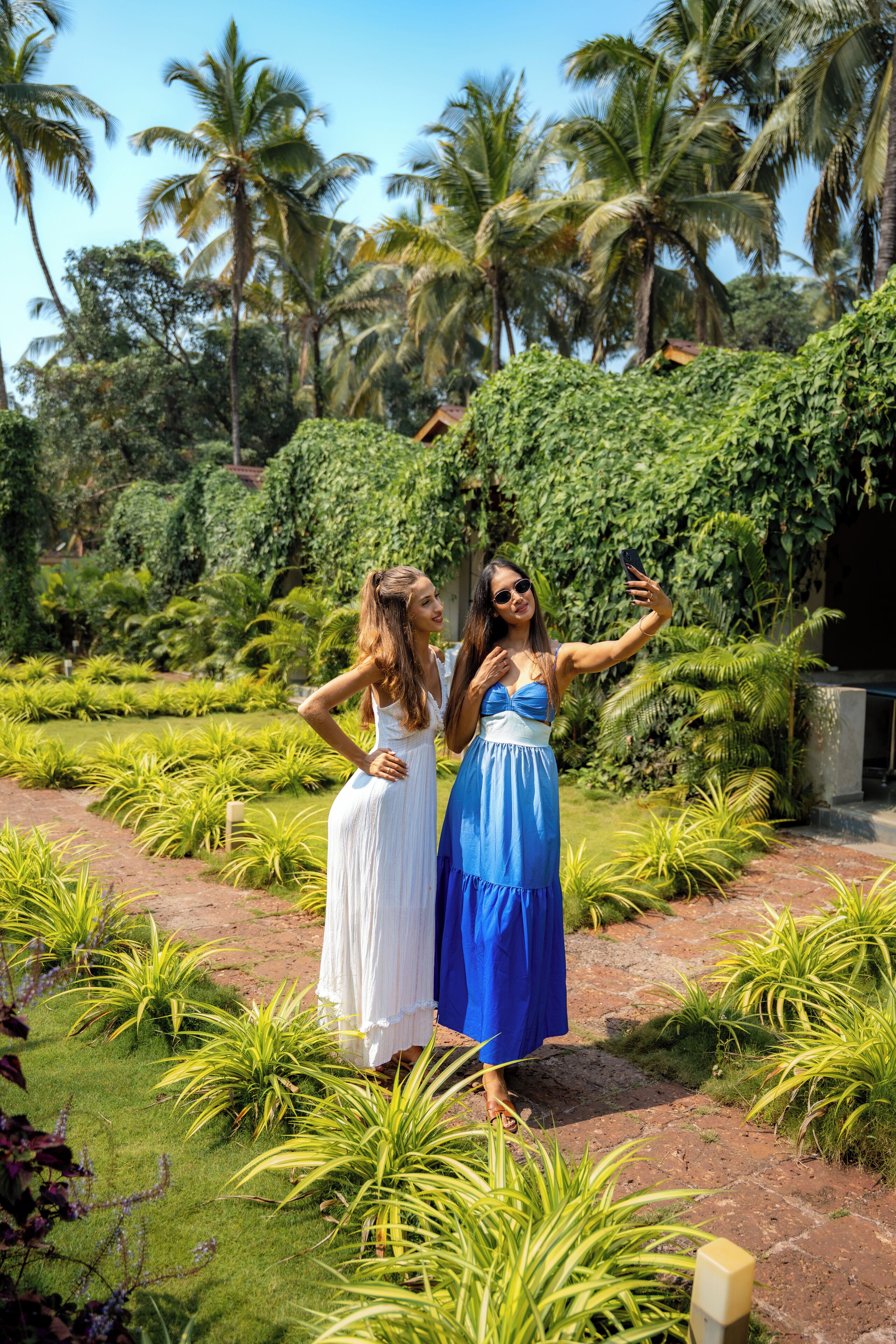 Two women in a garden with palm trees and a brick pathway.