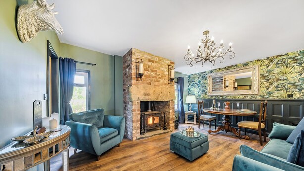 A cozy living room with a stone fireplace, plush seating, and a dining area with a table and chairs. - The Stables (Poulton-le-Fylde)