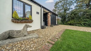 A white building with a stone sculpture, a gravel driveway, and a well-kept lawn. - The Stables (Poulton-le-Fylde)