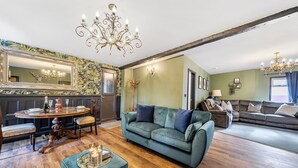 A spacious living room with a green sofa, a wooden dining table, and a chandelier. - The Stables (Poulton-le-Fylde)