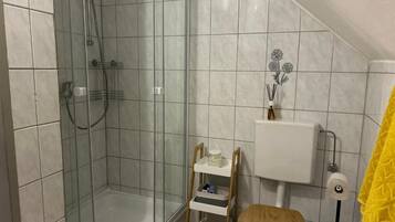 A bathroom with a glass-enclosed shower, a toilet with a wooden seat, and a white tiled wall.