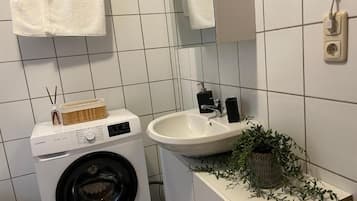 Un baño pequeño con lavadora, lavamanos y una planta en maceta.
