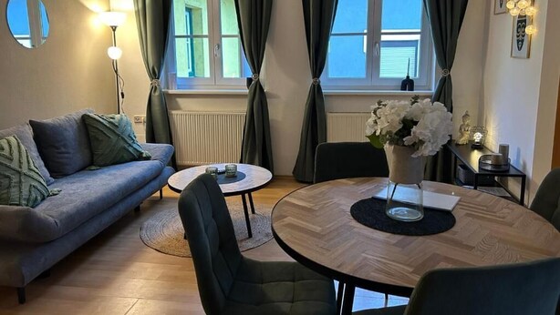 Uma sala de estar com sofá, mesa de centro, mesa de jantar, cadeiras e um vaso de flores.