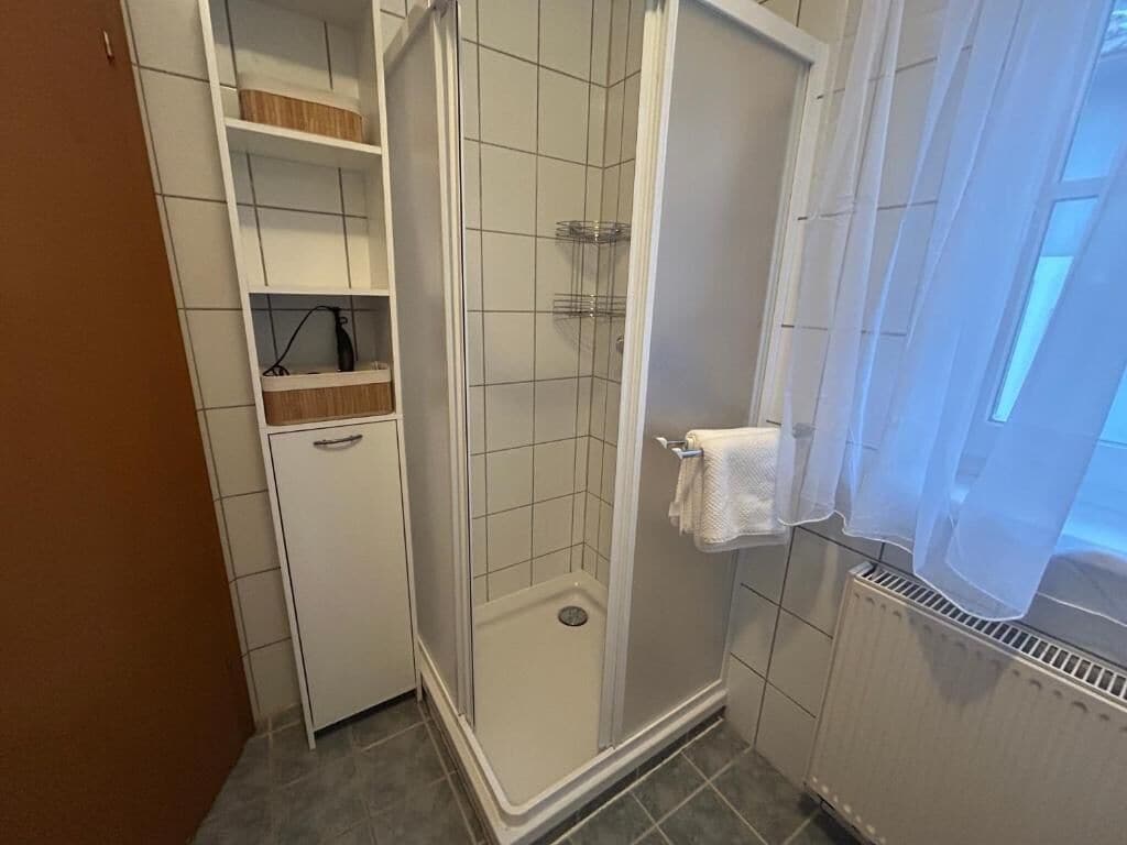 A bathroom with a shower, tiled walls, a white radiator, and a window with a view.