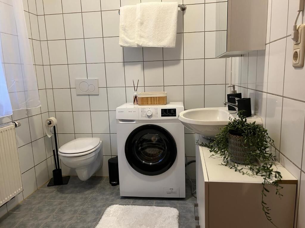 Ein kleines Badezimmer mit Toilette, Waschmaschine, Waschbecken und einem Blumentopf.