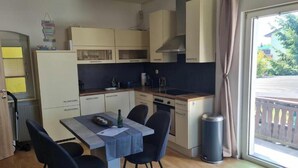 Uma cozinha compacta com uma mesa de jantar, cadeiras, um cesto de lixo e uma janela com vista.