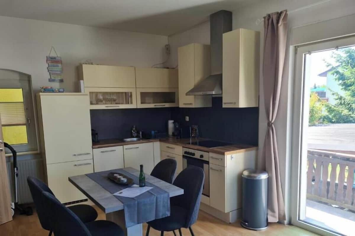 Una cocina compacta con una mesa de comedor, sillas, un cubo de basura y una ventana con vistas.
