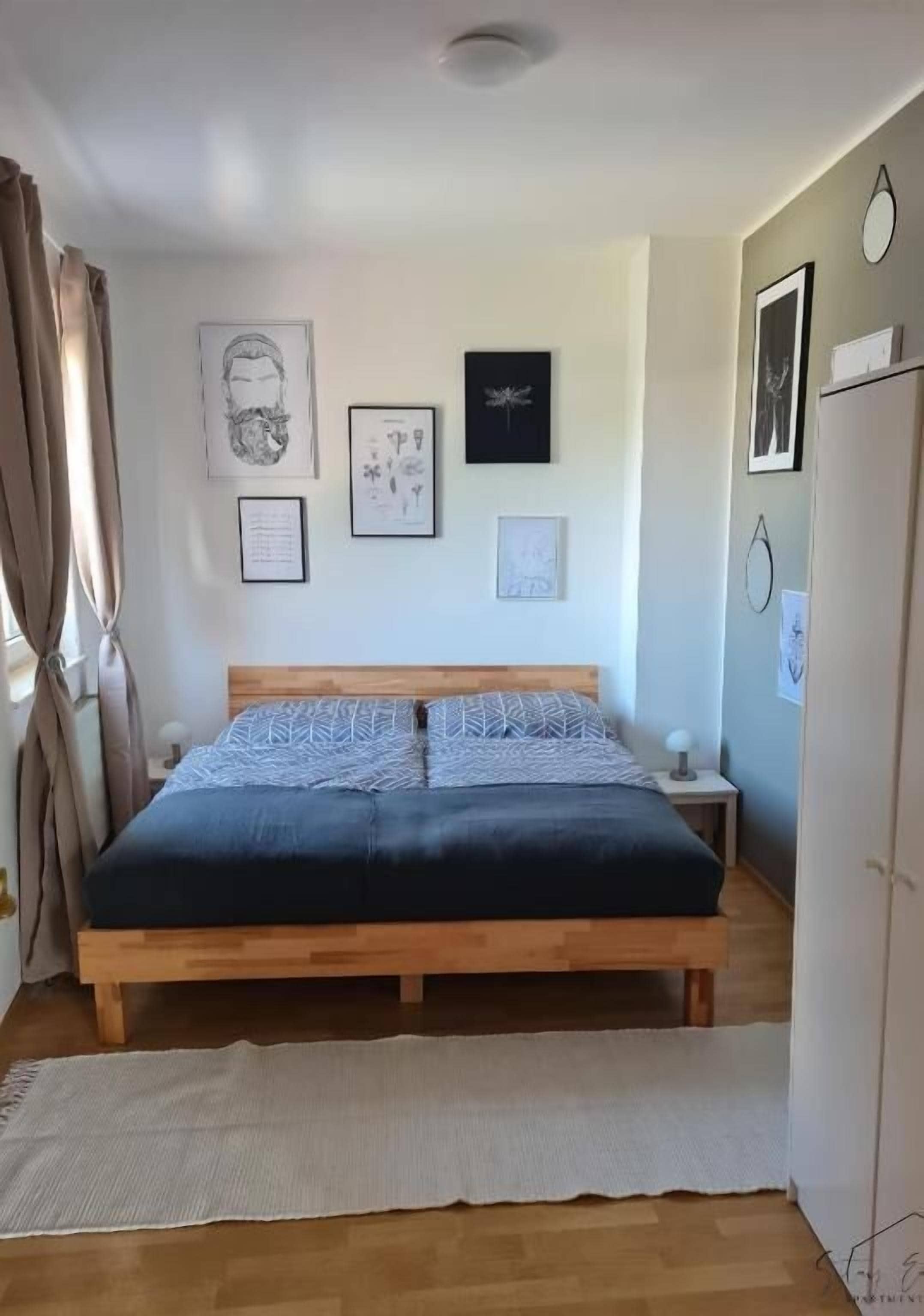 A bedroom with a wooden bed, a bedside table, a wall-mounted clock, and framed artwork.