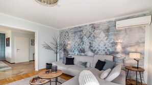 A modern living room with a grey sofa, a coffee table, and a wall-mounted air conditioner. - Baden Chalet – Black Forest Apartment with Panoramic Views in Bühl (Bühl)