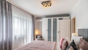 A bedroom with a bed, curtains, a chair, a wardrobe, and a ceiling light fixture. - Baden Chalet – Black Forest Apartment with Panoramic Views in Bühl (Bühl)
