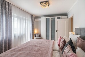 A bedroom with a bed, curtains, a chair, a wardrobe, and a ceiling light fixture.