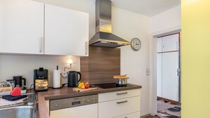 A modern kitchen with a dishwasher, a coffee machine, a kettle, and a pot of spaghetti. - Baden Chalet – Black Forest Apartment with Panoramic Views in Bühl (Bühl)