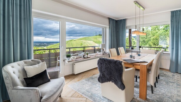A modern dining area with a large table, chairs, and a view of a green landscape through large windows. - Baden Chalet – Black Forest Apartment with Panoramic Views in Bühl (Bühl)