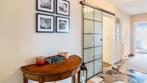 A hallway with a wooden table, framed floral artwork, a glass door, and a patterned floor. - Baden Chalet – Black Forest Apartment with Panoramic Views in Bühl (Bühl)