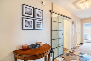 A hallway with a wooden table, framed floral artwork, a glass door, and a patterned floor.