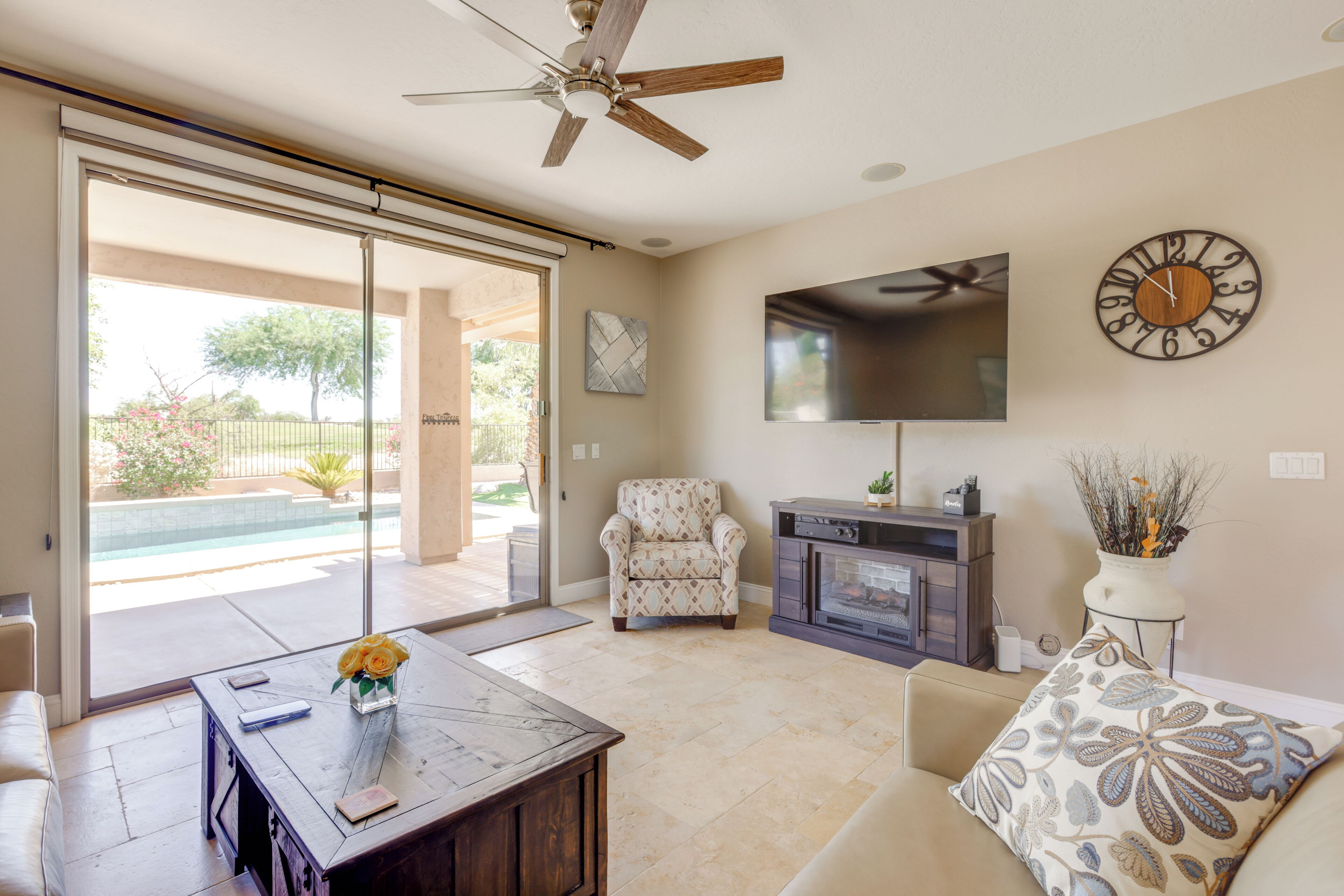A living room with a sofa, coffee table, TV, fireplace, and a view of a pool.