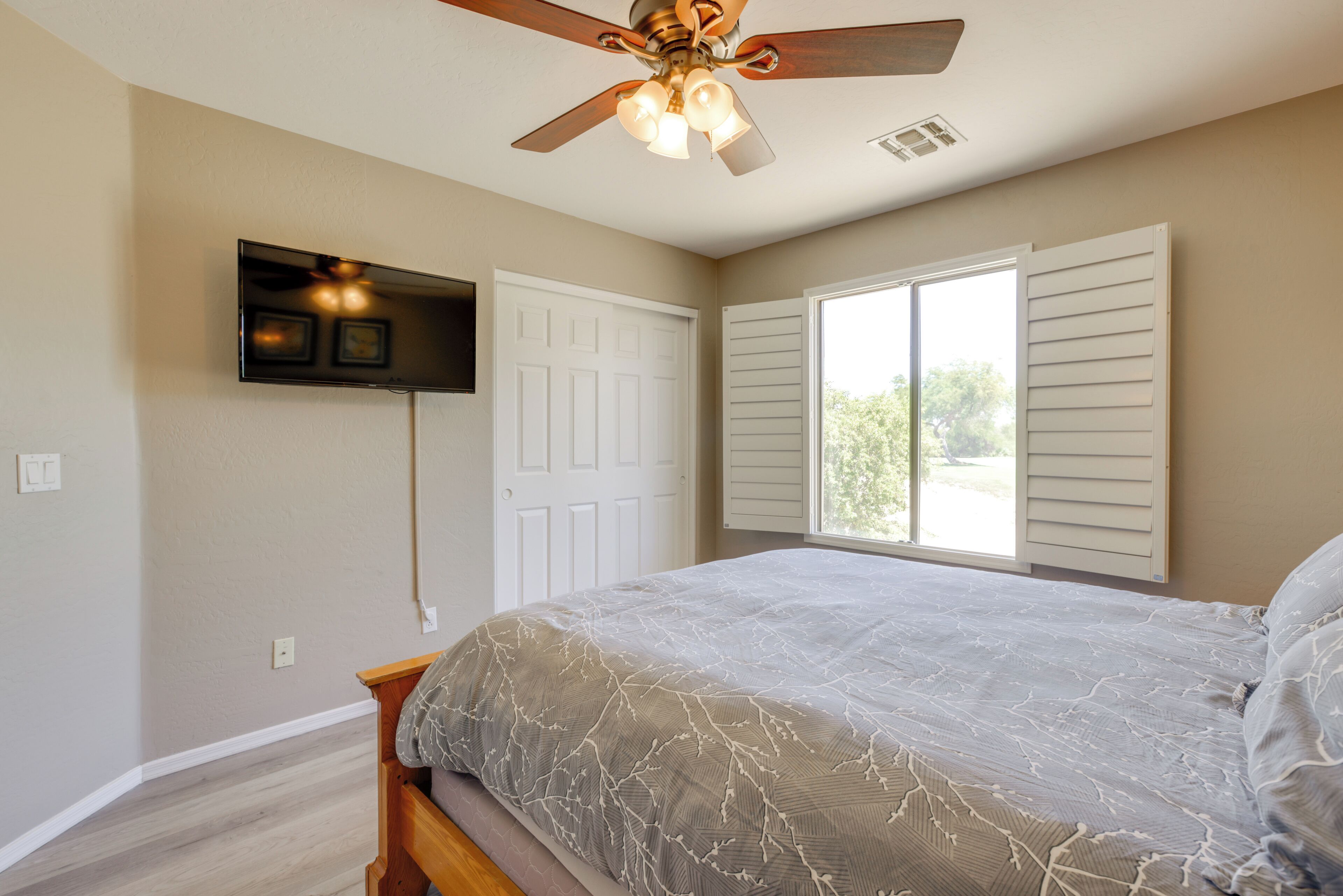 A bedroom with a bed, ceiling fan, and a TV mounted on the wall.