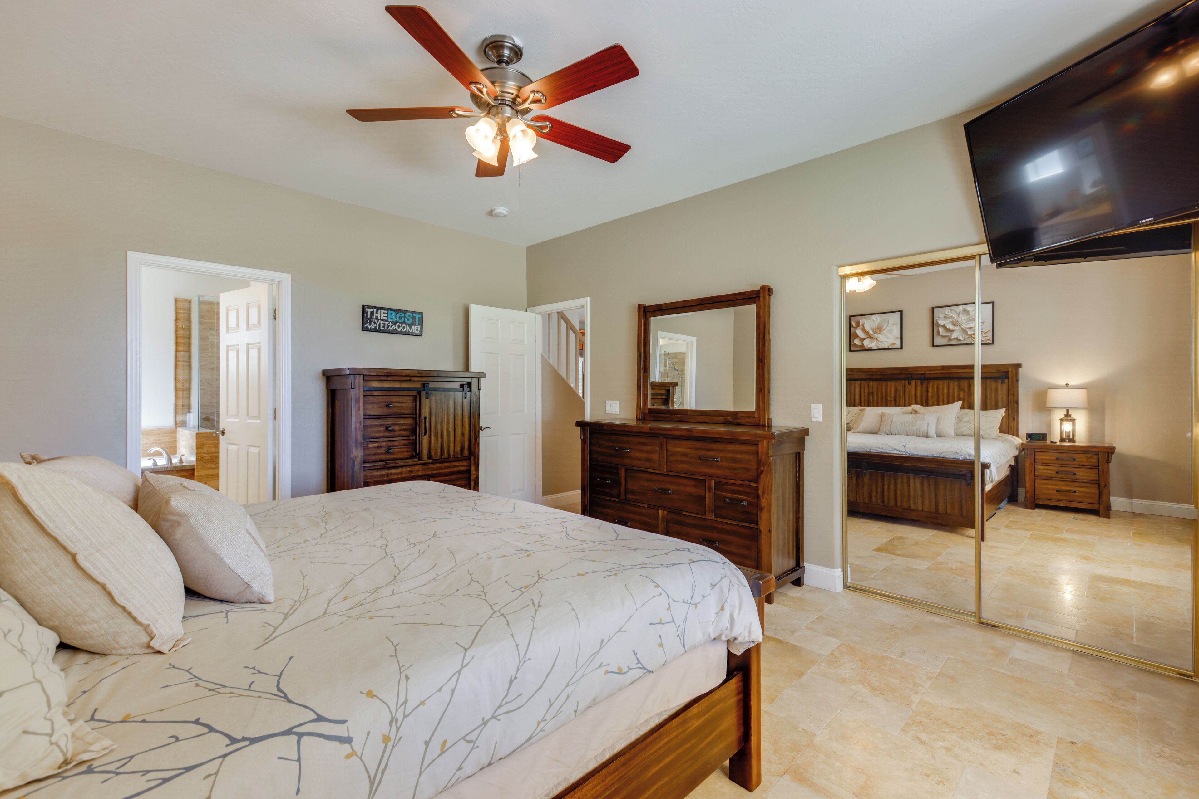 A bedroom with a bed, a dresser, a mirror, a ceiling fan, and a television.