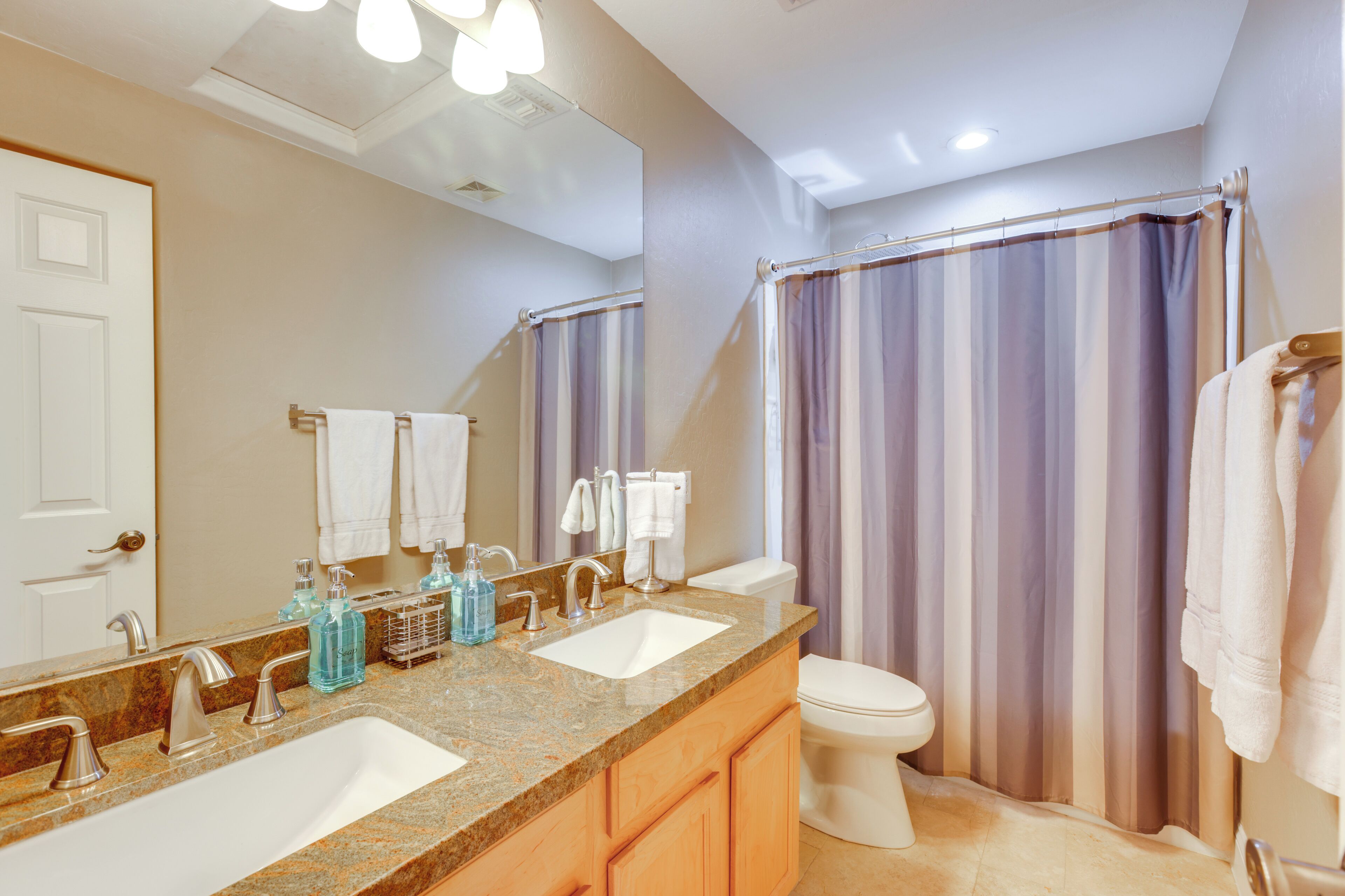 A bathroom with a double sink, a toilet, a shower curtain, and a mirror.