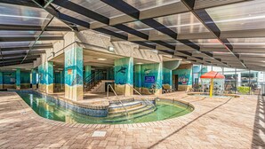 An indoor swimming pool with a tiled floor, a staircase leading to a higher level, and a covered area with a red umbrella. - Lighthouse Loft at Compass Cove - Unit 1151 (Myrtle Beach)