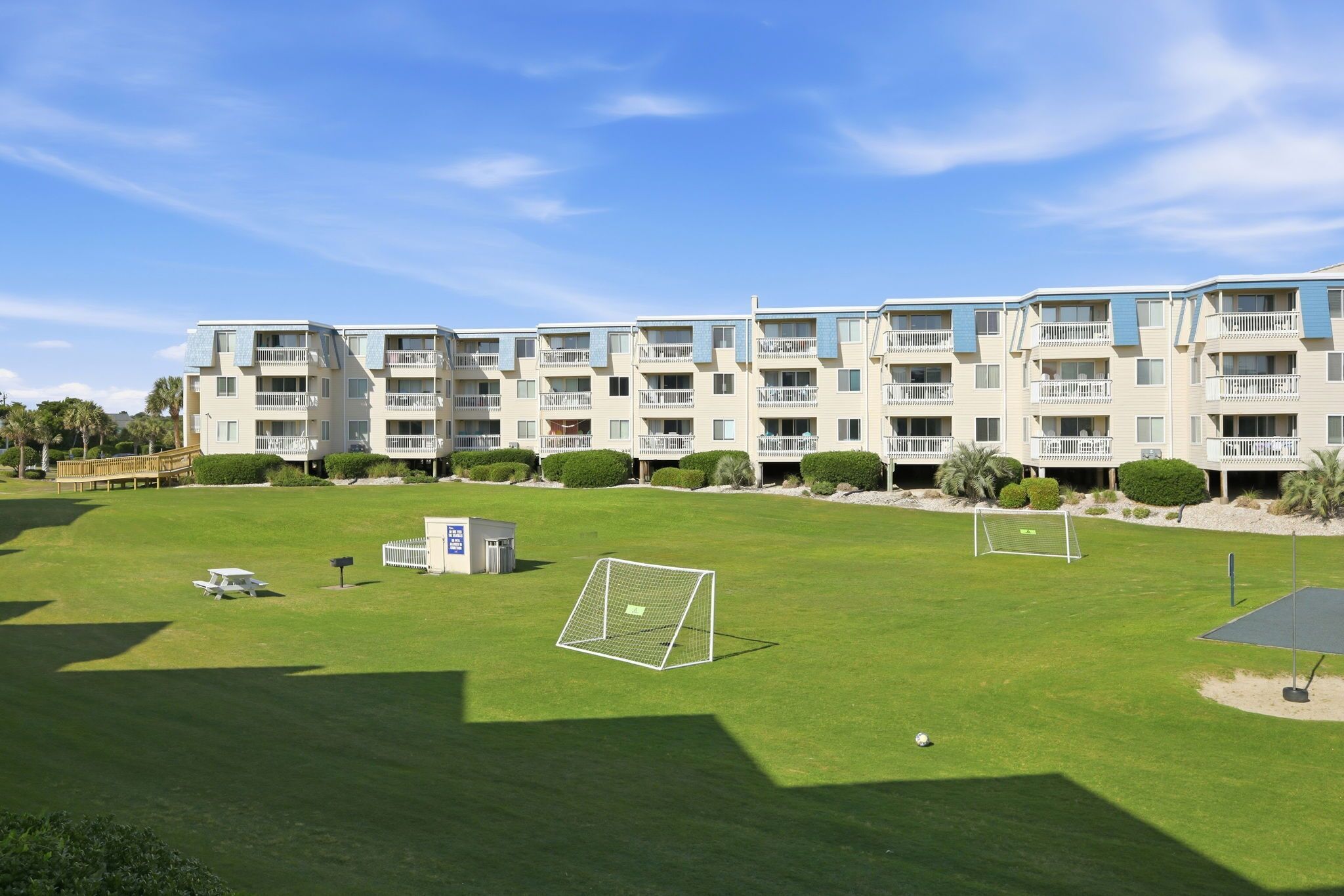 A multi-story residential building with balconies, a well-maintained lawn, and a soccer goal.