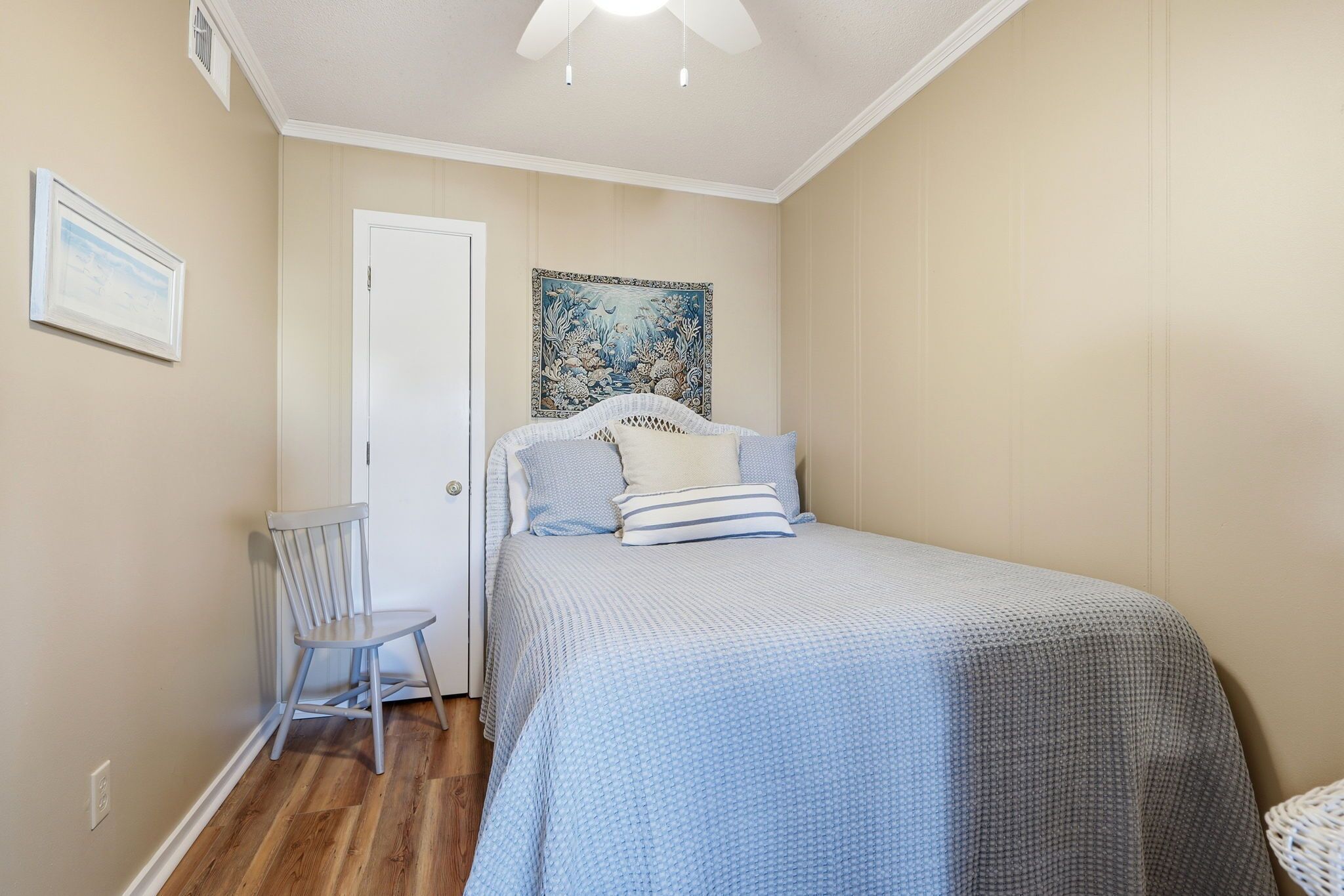 A bedroom with a bed, a chair, a door, and a wall painting.