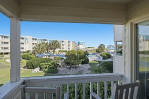 Un balcon donnant sur un espace paysager aménagé, comprenant une piscine et un ensemble d’immeubles.